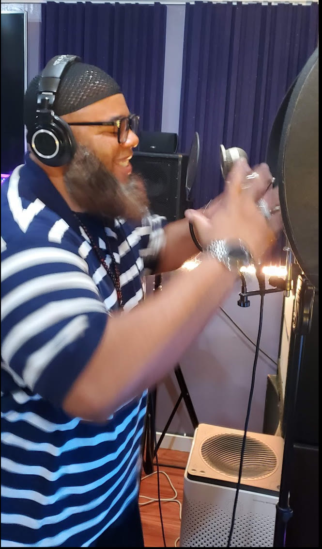Barrz tracking vocals in the booth, headphones on, hands on the mic shield